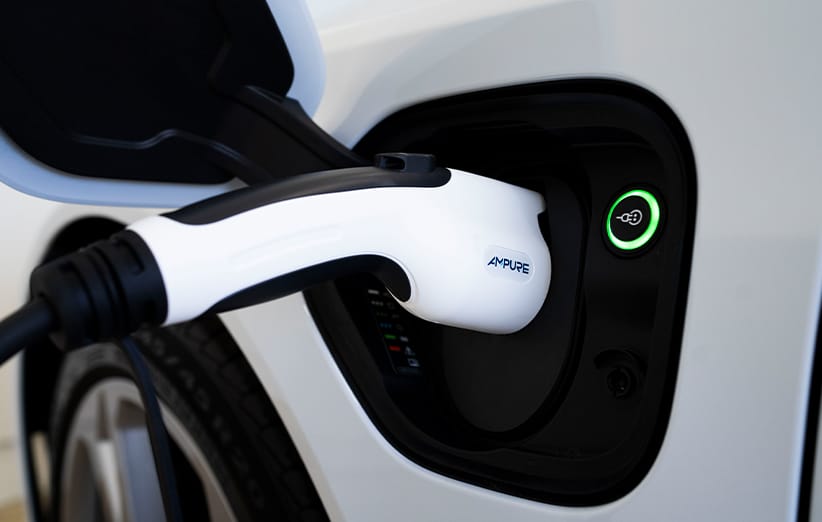 Close-up shot of the black and white Ampure Go portable charger for hybrid electric vehicles, capable of delivering Level 1 and Level 2 charging using standard 120V or 240V outlets, plugged into the open socket of a white Kia vehicle, with a green ring indicating active charging status.