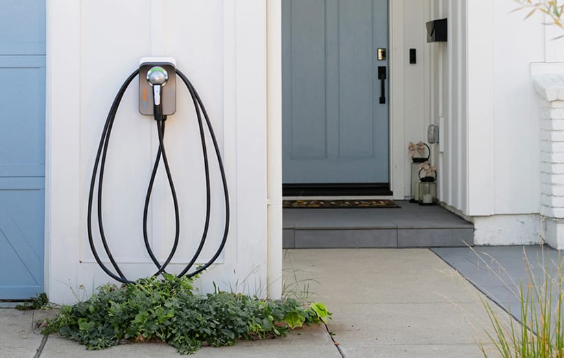Close-up shot of the black and white Ampure Go portable charger for hybrid electric vehicles, capable of delivering Level 1 and Level 2 charging using standard 120V or 240V outlets, plugged into the open socket of a white Kia vehicle, with a green ring indicating active charging status.