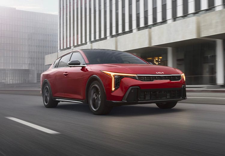 Dynamic shot of the 2026 Kia K4 sedan in red, looking stylish as it drives through an urban city environment