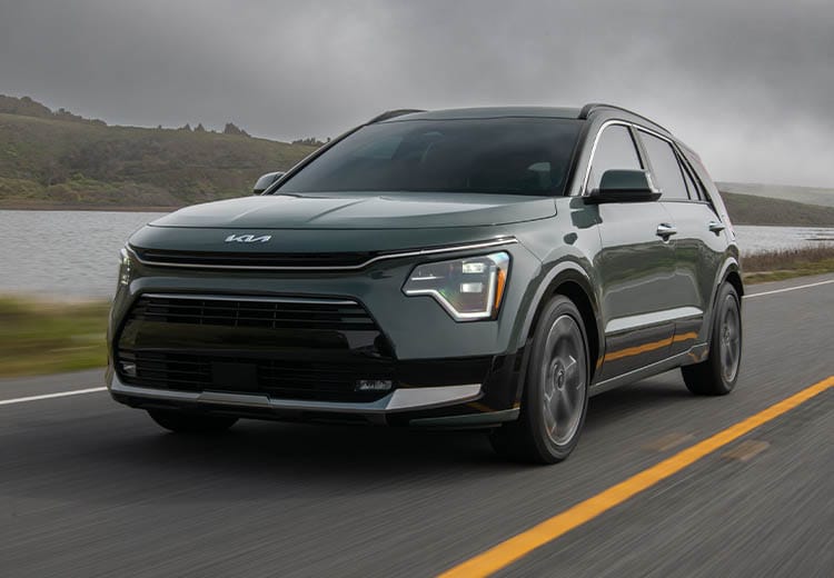 2026 Kia Niro Hybrid in green, three-quarter back view, driving on a road by a hill