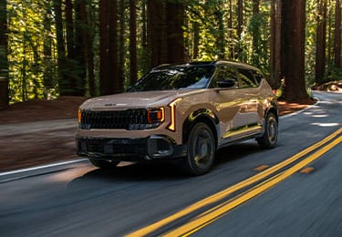 Shot of the 2027 Kia Seltos in brown driving quickly through a winding forest road. The image is highlighting the compact SUVs bold front grille, tinted windshield, and LED headlights.