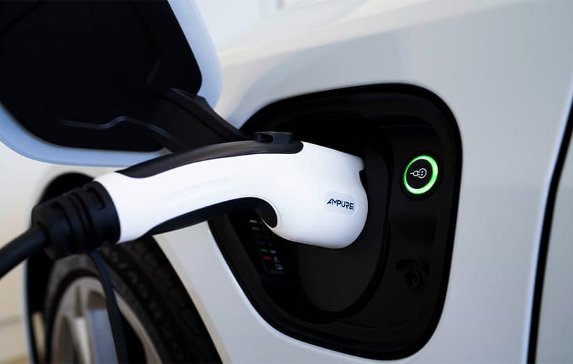 Close-up shot of the black and white Ampure Go portable charger for electric vehicles, capable of delivering Level 1 and Level 2 charging using standard 120V or 240V outlets, plugged into the open socket of a white Kia vehicle, with a green ring indicating active charging status.